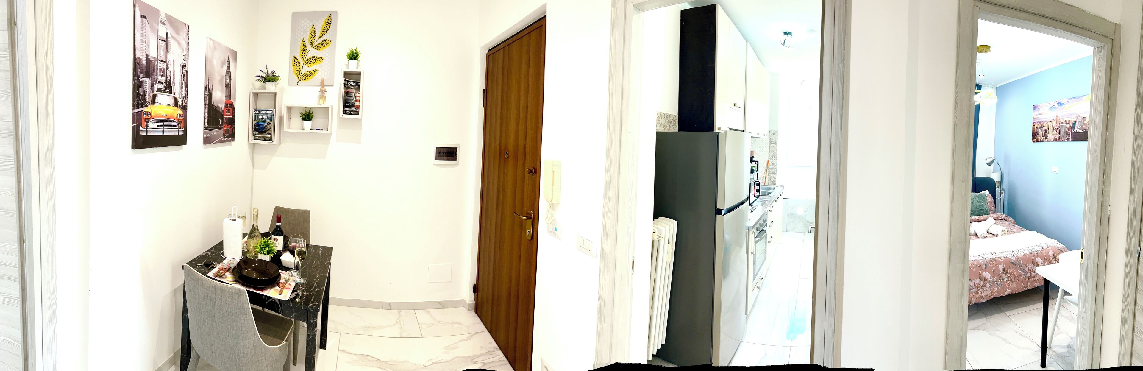 Un pasillo con una zona de comedor, una puerta de madera y una cama en la habitación contigua con pared azul.