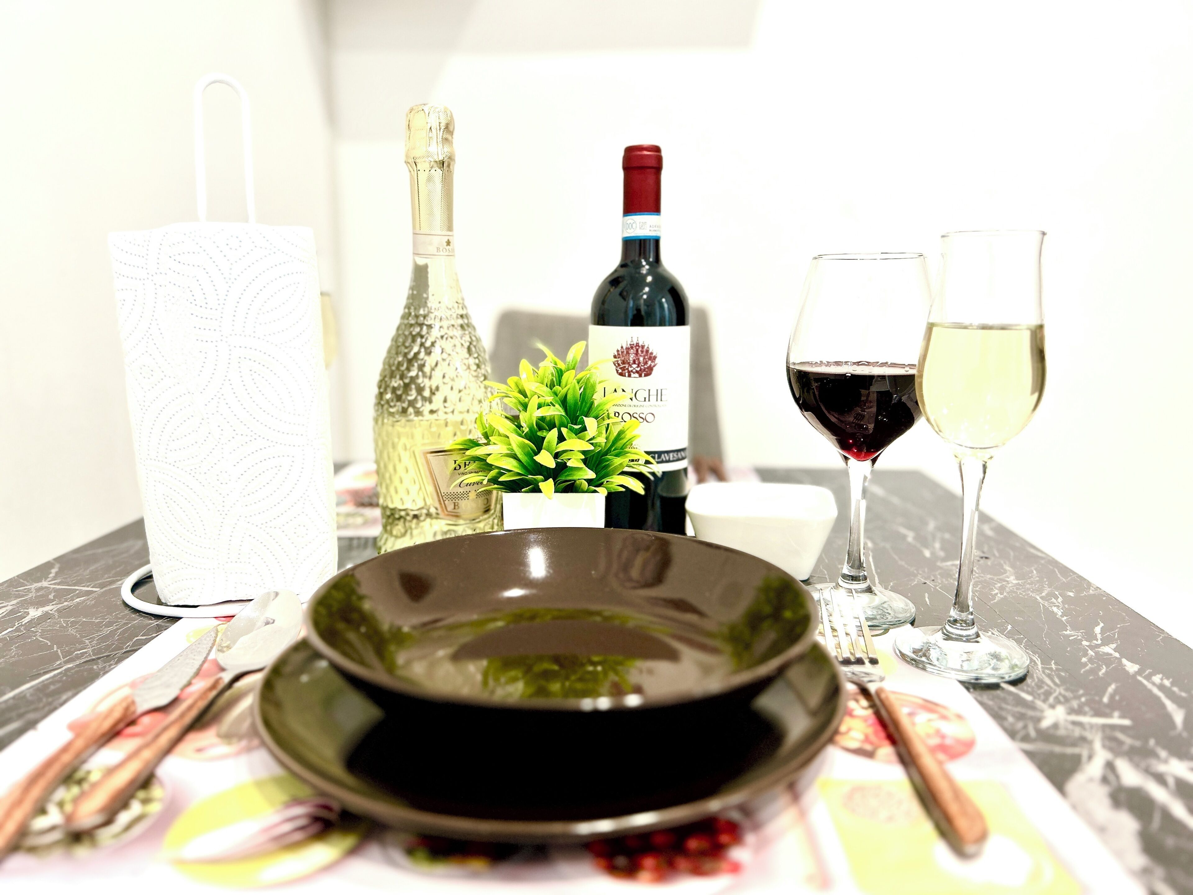 Ein Tisch gedeckt mit einer Schüssel, Weinflaschen, Gläsern und einer Papiertuchrolle.