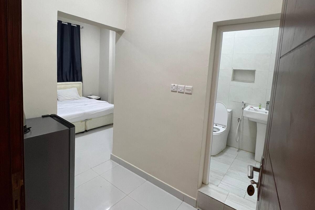 A compact hotel room with a bed, a small desk, a bathroom with a toilet and sink, and a shower area.