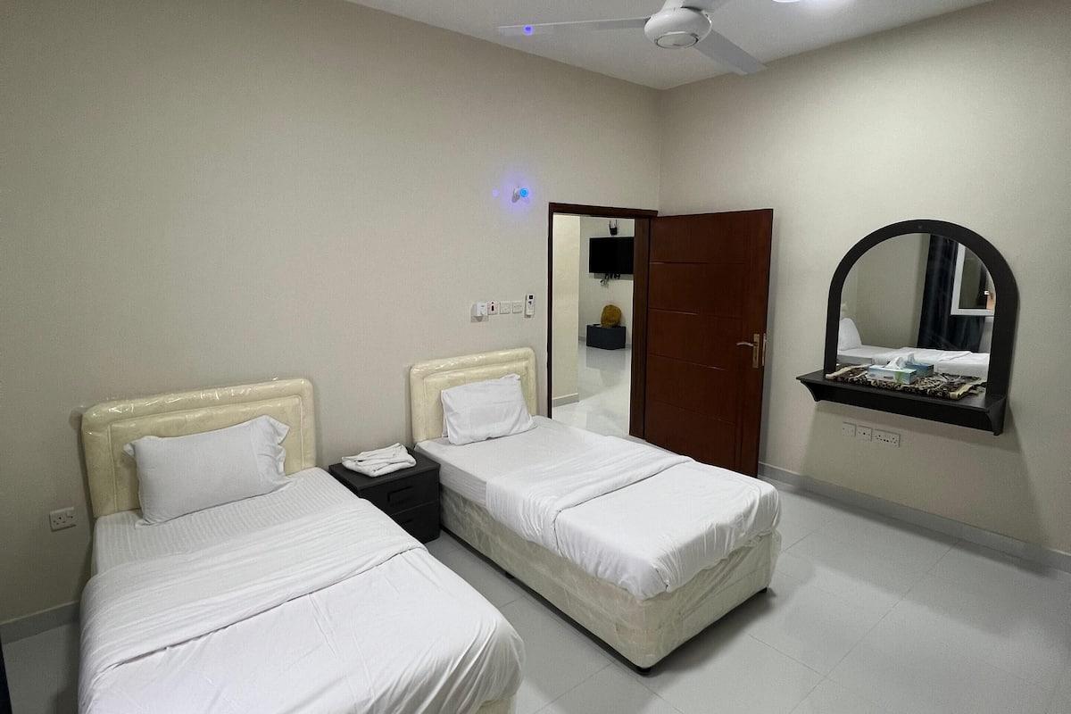 A hotel room with two beds, a ceiling fan, a mirror, and a door.