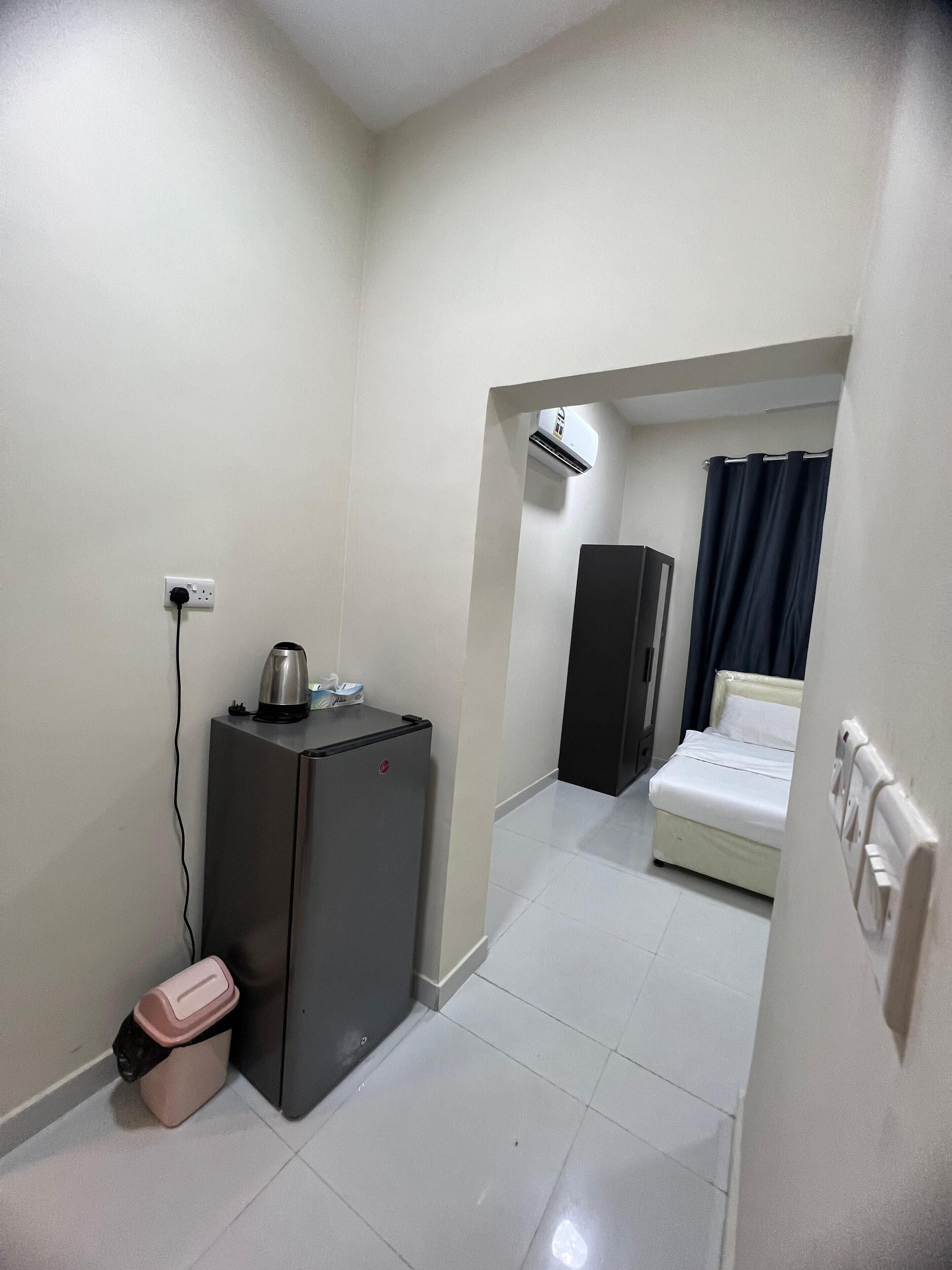 A compact room with a kitchenette area, a bed, and a dark-colored wardrobe.