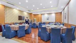 Une salle de conférence avec plusieurs tables rondes, des chaises bleues et un téléviseur fixé au mur.