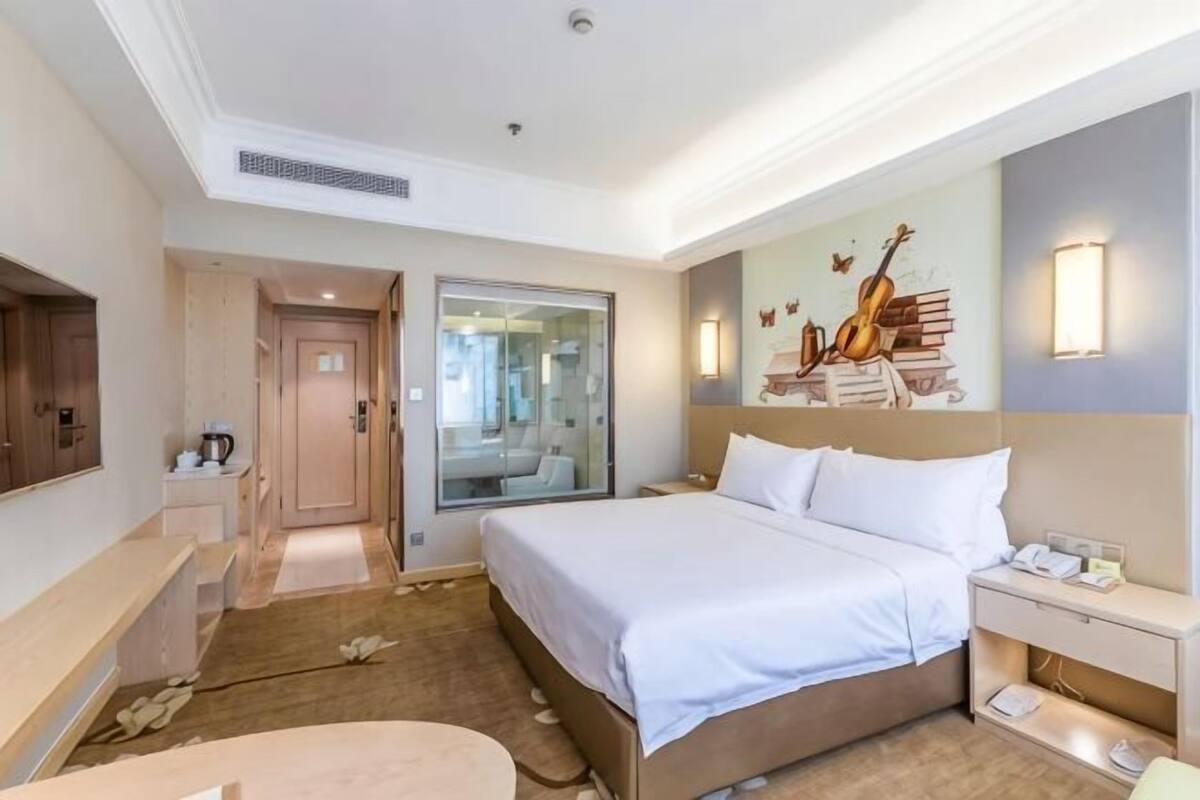 Een hotelkamer met een groot bed, nachtkastjes, een bureau, een spiegel en een aan de muur bevestigde gitaardecoratie.
