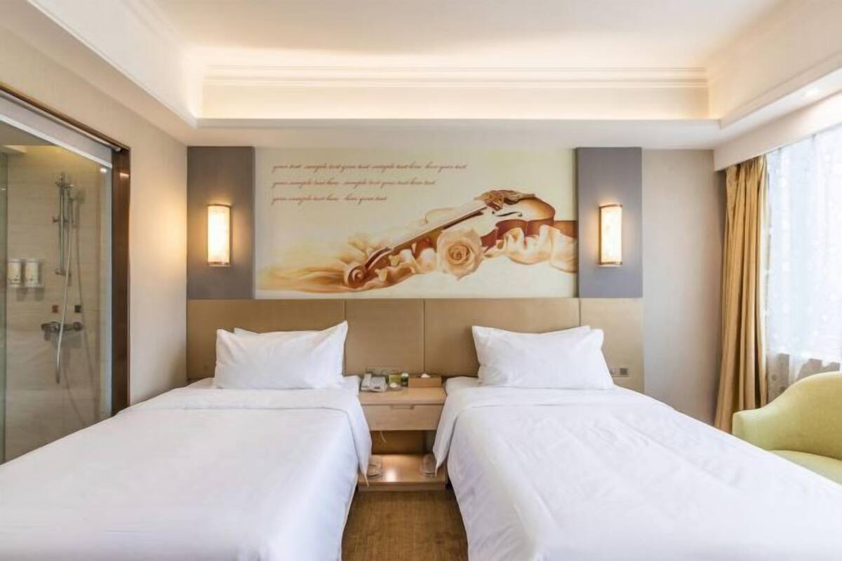 Een hotelkamer met twee bedden, een douche, een aan de muur hangend kunstwerk en een raam met gordijnen.