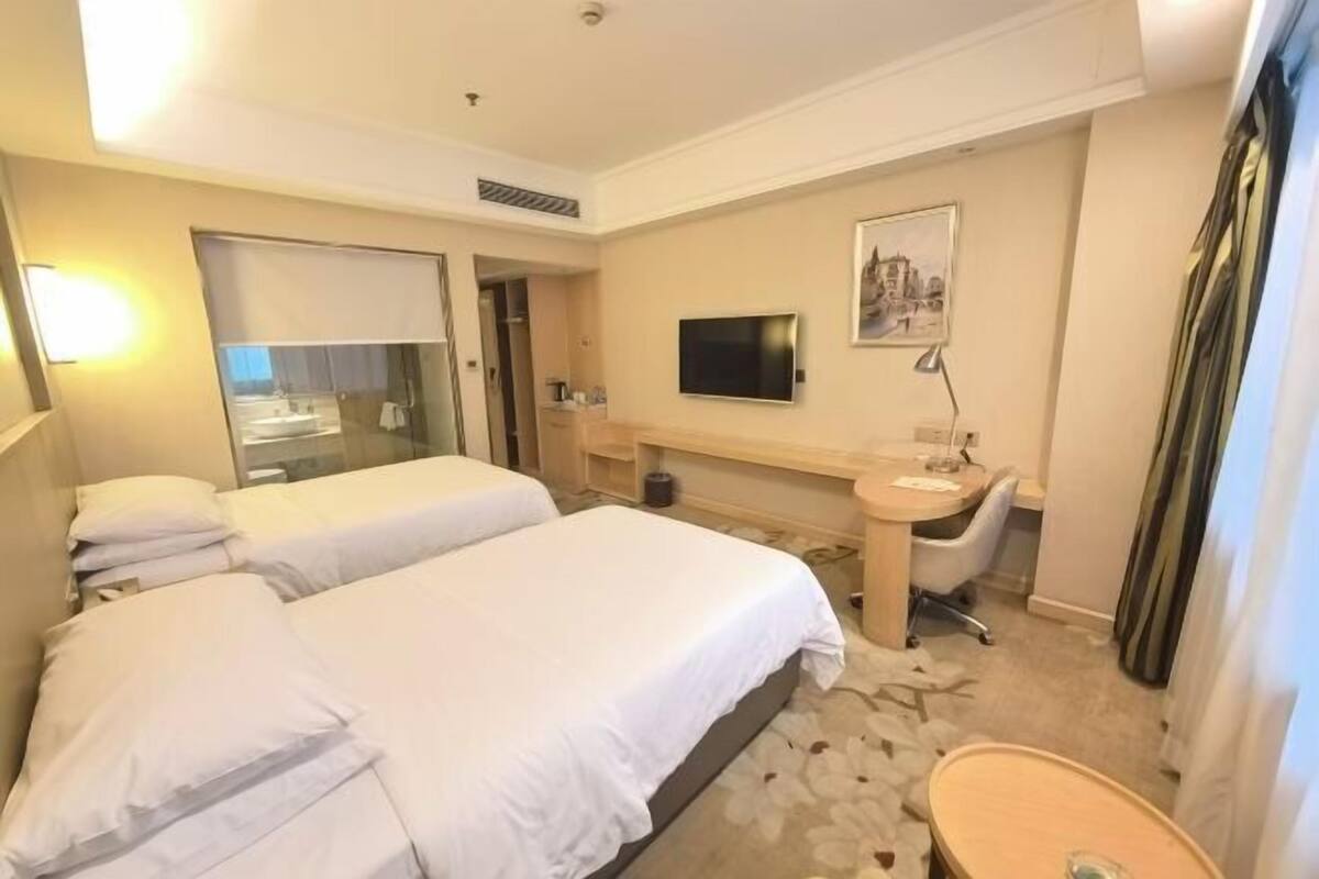 Een hotelkamer met twee bedden, een bureau, een stoel, een televisie, een spiegel en een badkamer.