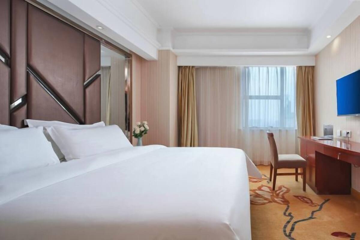 Een hotelkamer met een groot bed, een bureau, een stoel, een televisie en een raam met gordijnen.