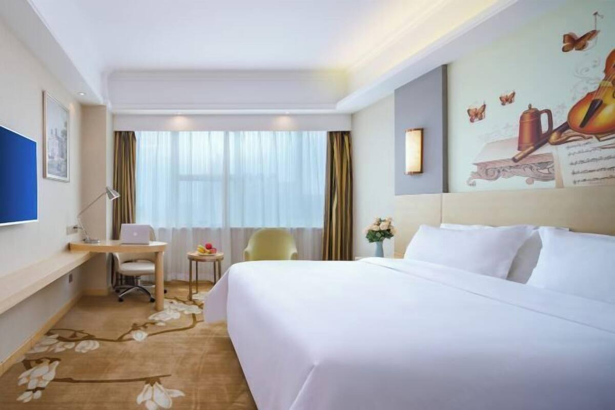 Een hotelkamer met een bed, bureau, stoel en raam met gordijnen.