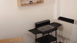 A room with a wooden chair, a small black table with a grill, and two wooden shelves on the wall. - Tranquil apartment in Caprara with stunning views (Caprara)