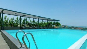 A swimming pool with a metal railing, surrounded by lounge chairs and a covered area with a view of the cityscape. - Snug three-bedroom Unit (Accra)