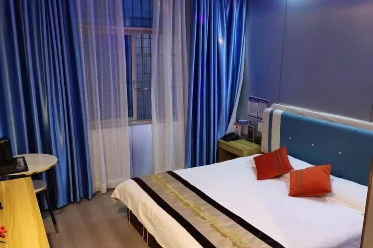 Una habitación de hotel con cama, cortinas, mesita de noche y velador.