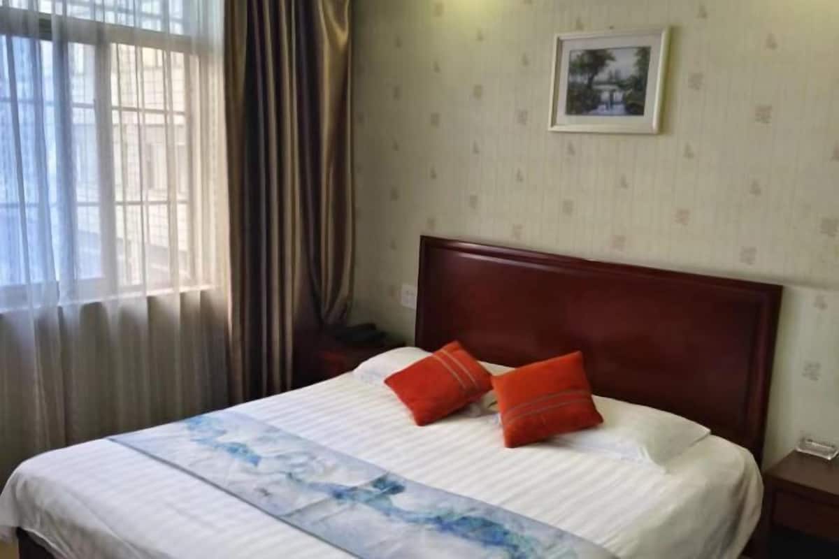Una habitación de hotel con cama, cortinas, un cuadro en la pared y una mesita de noche.
