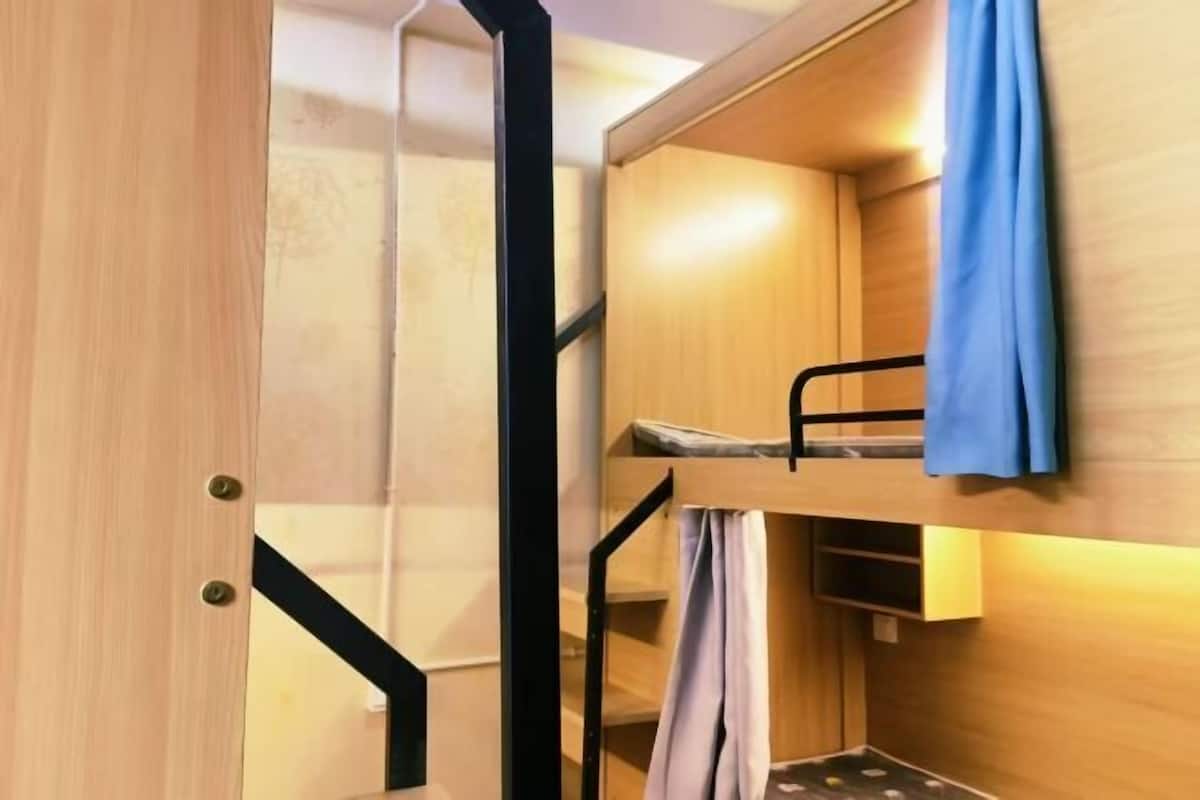 Una cama litera con estructura de madera, una pequeña repisa y una cortina.