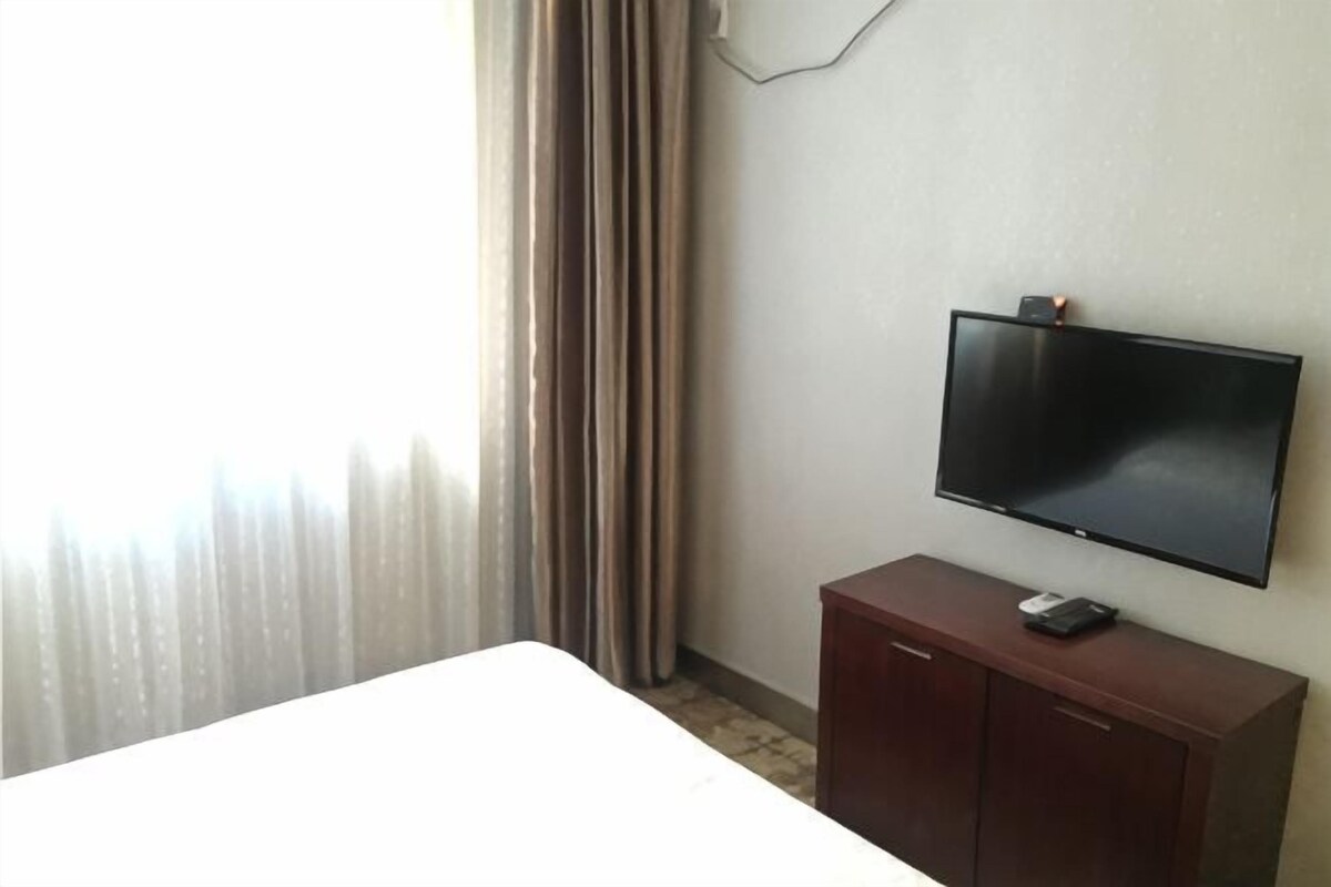 A hotel room with a bed, a television mounted on a wall, and a wooden cabinet.