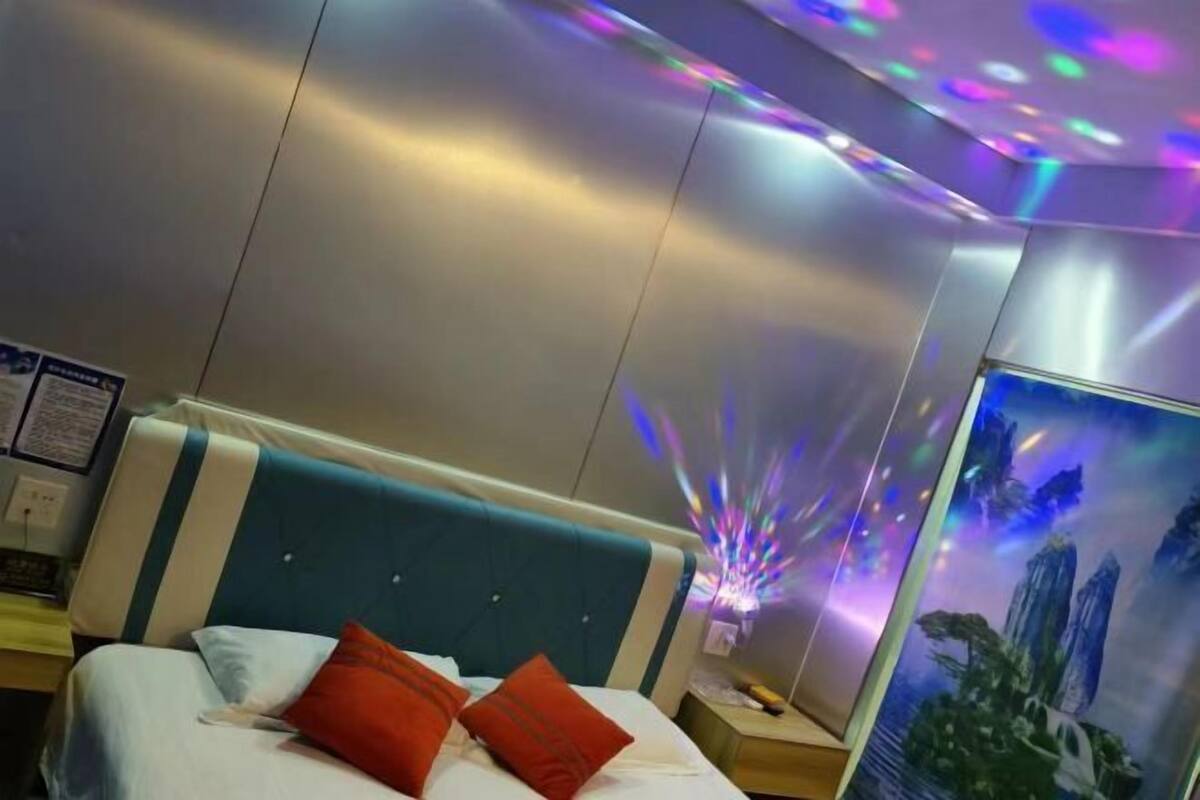 Una habitación de hotel con cama, mesita de noche, televisor montado en la pared y un cartel.