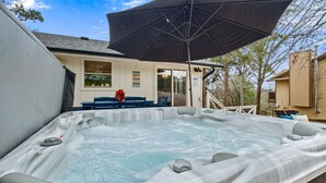 A hot tub with a large umbrella, surrounded by a deck with chairs and a small table.