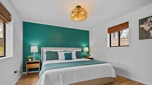 A bedroom with a large bed, teal accent walls, a wooden floor, and a hanging light fixture.