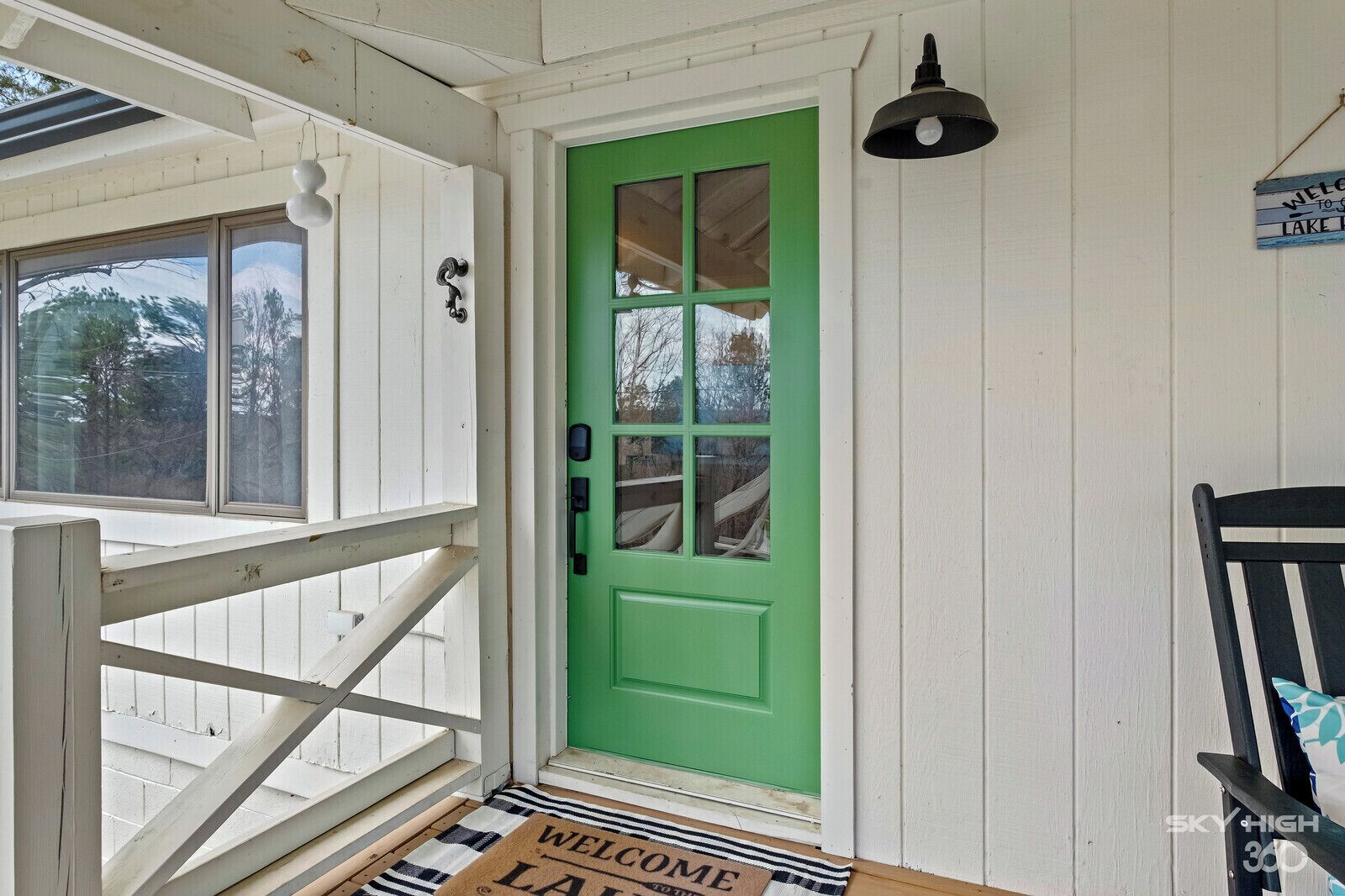 A green door with a window, a white porch railing, and a welcome mat.