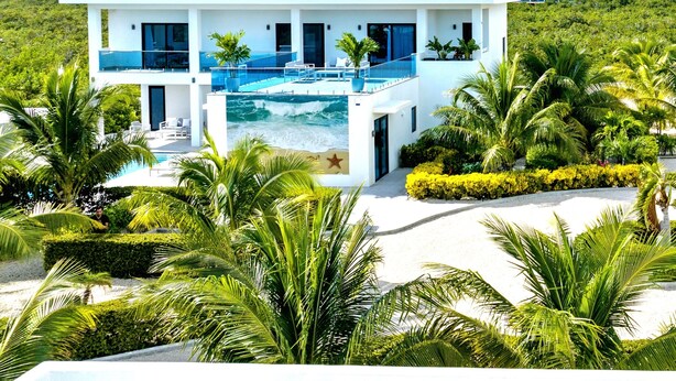 Une maison moderne à deux étages, dotée d’une piscine, entourée d’une végétation luxuriante et de palmiers.