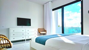 Une chambre à coucher comprenant un lit, une télévision, une commode, une chaise et une grande fenêtre donnant sur un beau paysage.