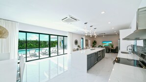 Une cuisine moderne dotée d’un grand îlot central, un coin repas avec vue sur une piscine et un espace de vie avec un téléviseur.