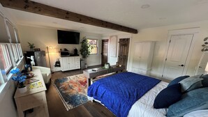 A bedroom with a large bed, wooden flooring, a desk with a computer, a TV, and a wardrobe.