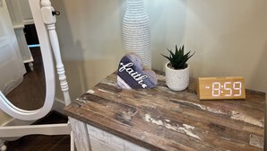 A rustic wooden nightstand with a white lamp, a small potted plant, a decorative sign, and a digital clock displaying 8:59 PM.