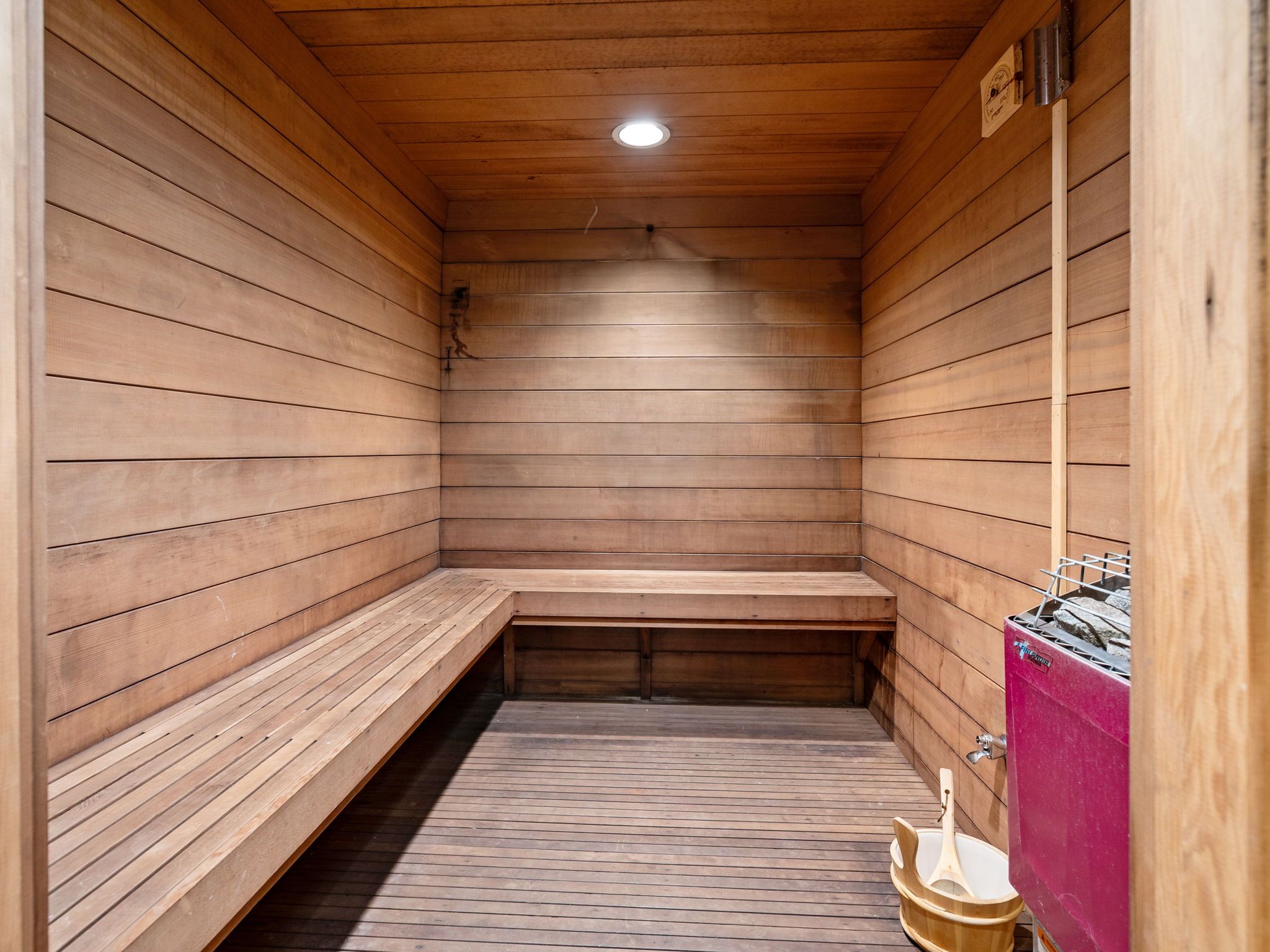 Una sauna con paredes y bancos de madera, una luz en el techo y un generador de vapor.