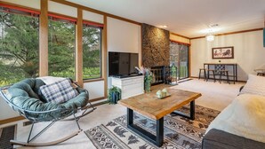 A modern living room with a large window, a television, a fireplace, and a dining area.