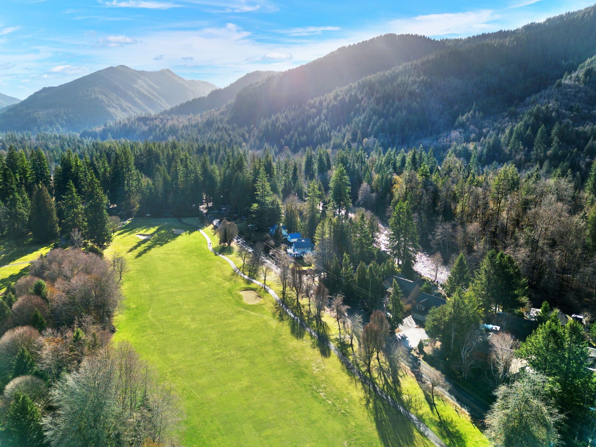 A mountainous landscape with a golf course, dense forests, and a few buildings.