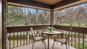 A covered outdoor seating area with a table and chairs, overlooking a landscaped garden and trees.