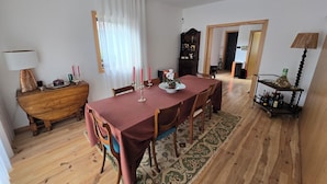 Un comedor con una mesa de madera dispuesta para cuatro personas, un armario de madera y una pequeña mesita con una lámpara.