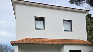 Un edificio de dos pisos con techo de tejas, un patio cubierto con un banco y una mesa, y una puerta que da al interior.