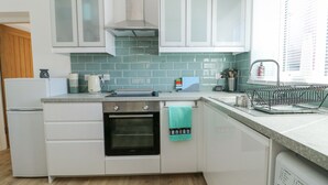 A modern kitchen with white cabinets, a built-in oven, a coffee maker, and a dish rack. - Cornel Clud (Cemaes Bay)