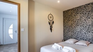 A bedroom with a bed, a dreamcatcher, patterned wallpaper, and a door with a semi-circular window.