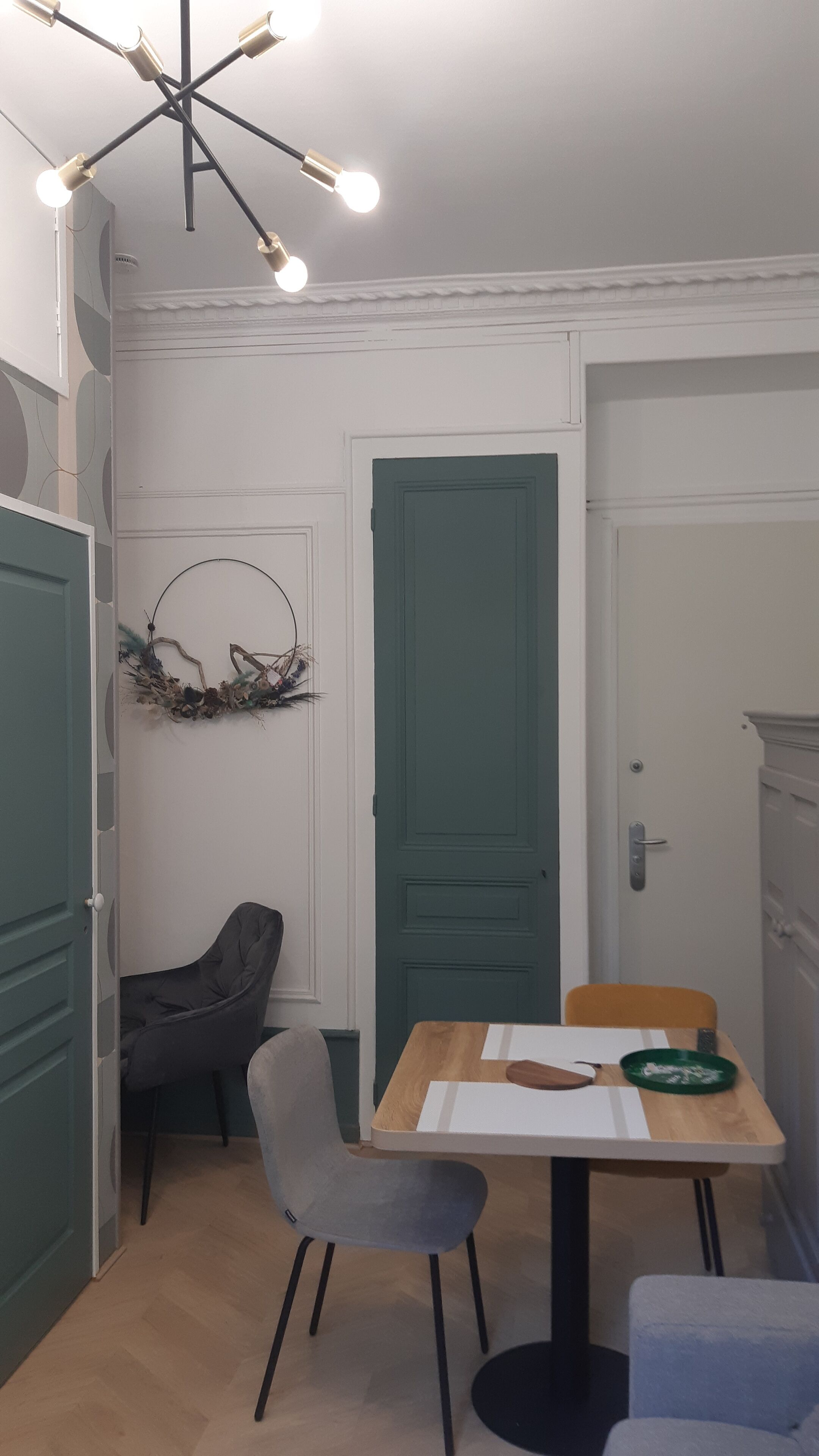 Un petit coin repas avec une table, deux chaises, une couronne décorative et une porte verte.