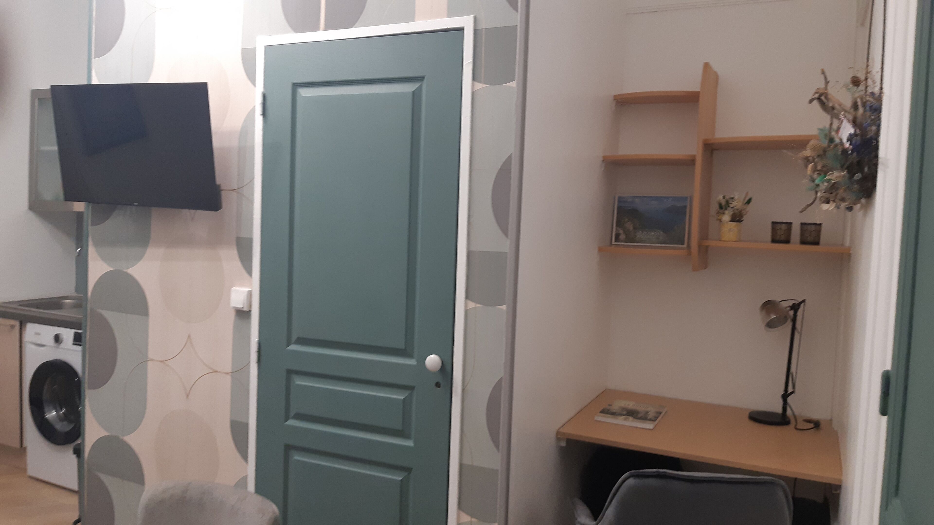 Una stanza con lavatrice, televisione a muro, una scrivania con sedia e una porta.