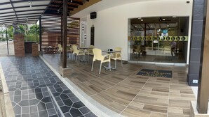 An outdoor seating area with hexagonal tiles, a covered patio with a striped roof, and a glass entrance to a restaurant. - Hotel Roma Urabá (Apartadó)