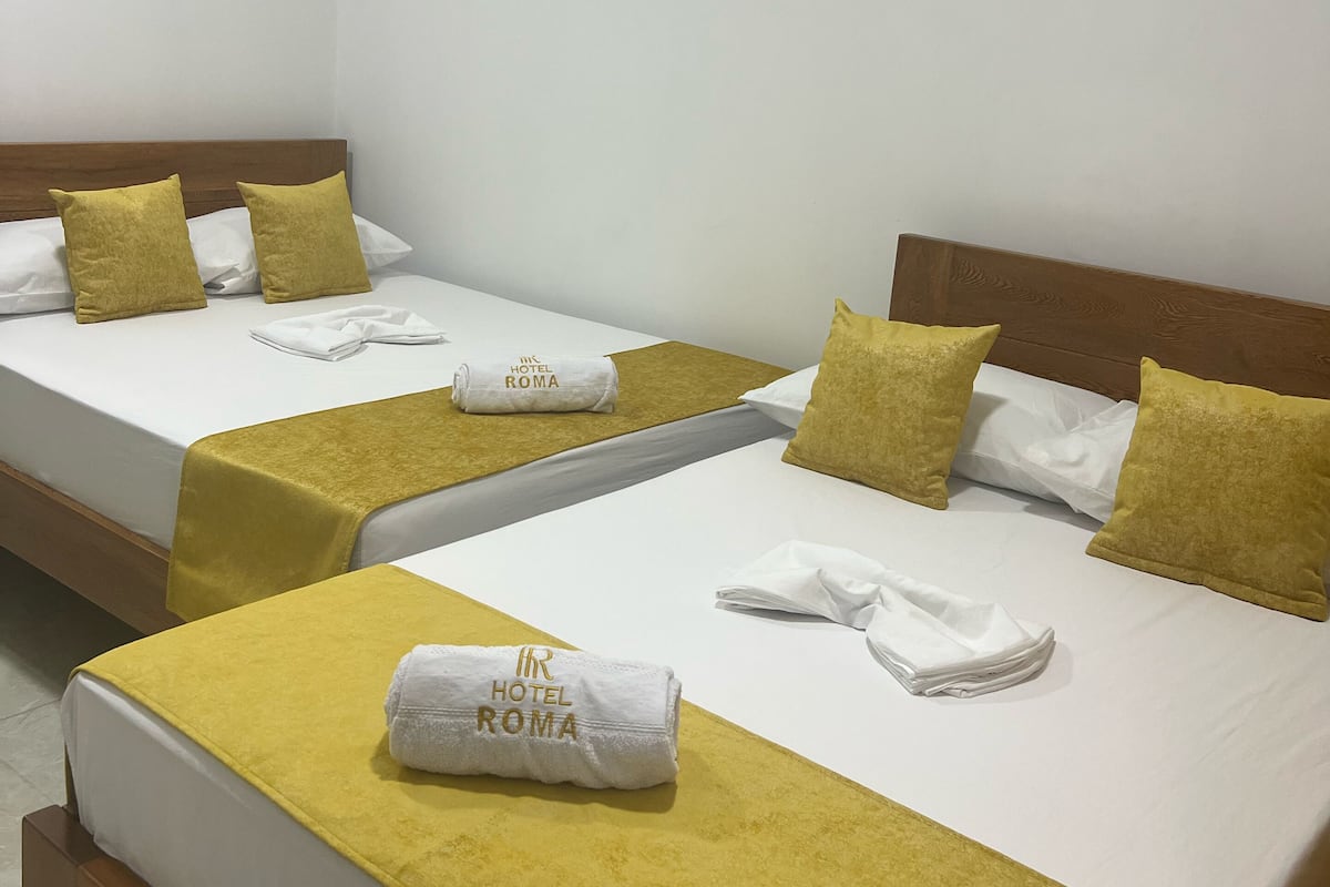 A hotel room with two beds, each with a yellow bedspread and white linens. There is an air conditioning unit on the wall above the beds.