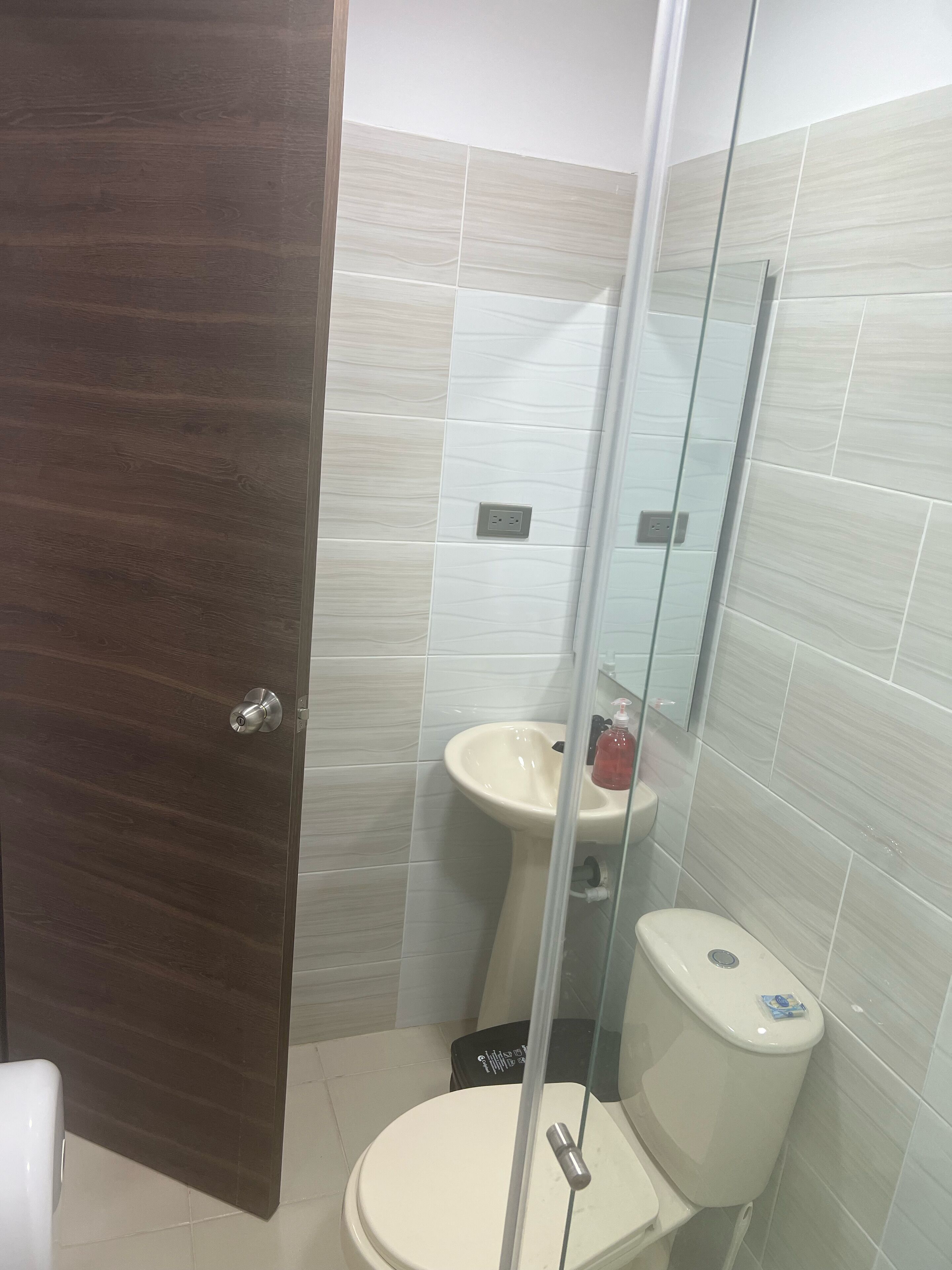 Un baño con puerta de madera, lavamanos, inodoro y cabina de ducha de vidrio.