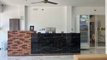 A reception area with a marble counter, a ceiling fan, a refrigerator, and a vending machine.