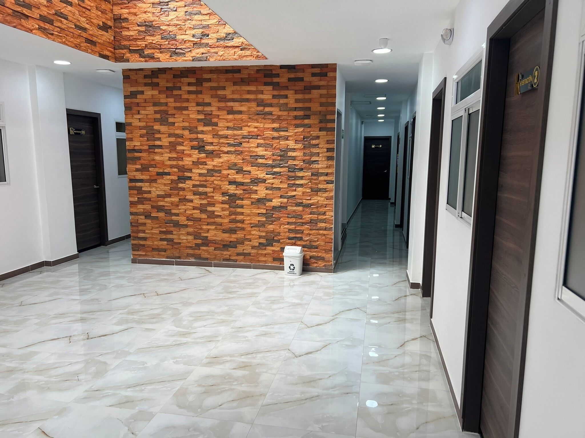 A hallway with a marble floor, a brick-patterned wall, and a door with a sign.