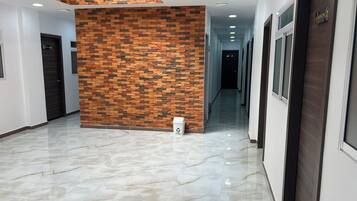 A hallway with a marble floor, a brick-patterned wall, and a door with a sign.