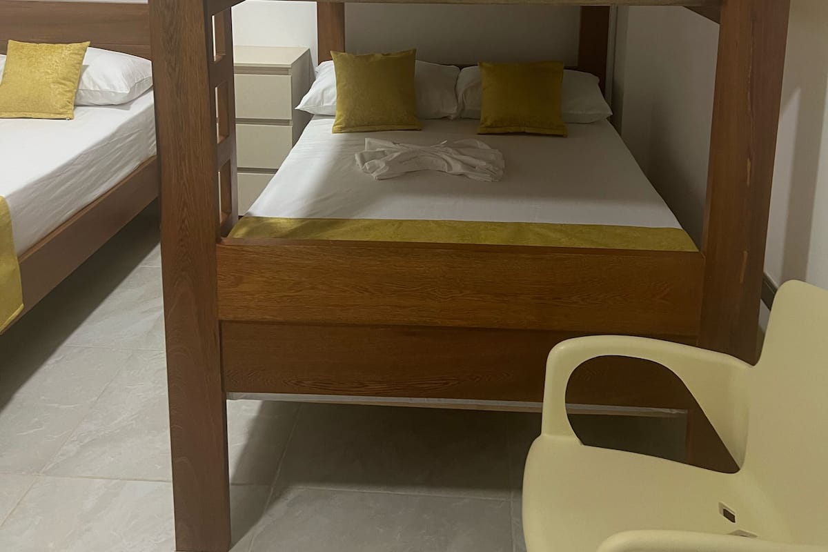 A bunk bed with a wooden frame, two beds with white bedding and yellow pillows, and a white chair.