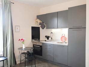 Una cocina compacta con gabinetes grises, una pequeña mesa de comedor, una cafetera y un lavamanos.