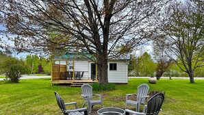 A small cabin with a deck, surrounded by a grassy yard and trees. There are Adirondack chairs and a metal fire pit. - Charming 3-bedroom house in Trout Lake close to trails & lakes. (Trout Lake)