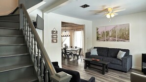 A spacious living room with a dark grey sofa, a coffee table, and a staircase with wooden railings. - Charming 3-bedroom house in Trout Lake close to trails & lakes. (Trout Lake)