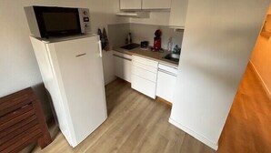 Eine kleine Küche mit weißen Schränken, einer Mikrowelle, einem Spülbecken und einer roten Kaffeemaschine.