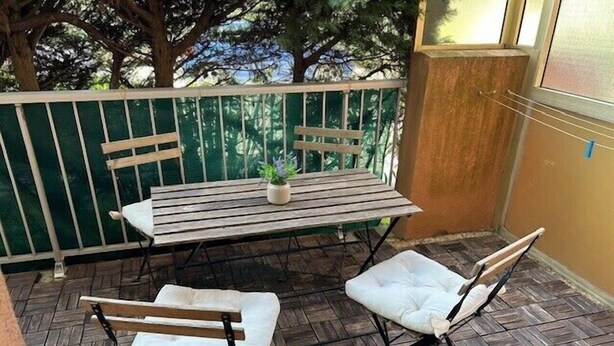 Eine Terrasse mit einem Holztisch und zwei gepolsterten Stühlen, einem Blumentopf und einem grünen Geländer.