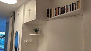 Ein Zimmer mit einem weißen Kleiderschrank, einer kleinen Bücherablage, einem Blumentopf und einem runden Spiegel.