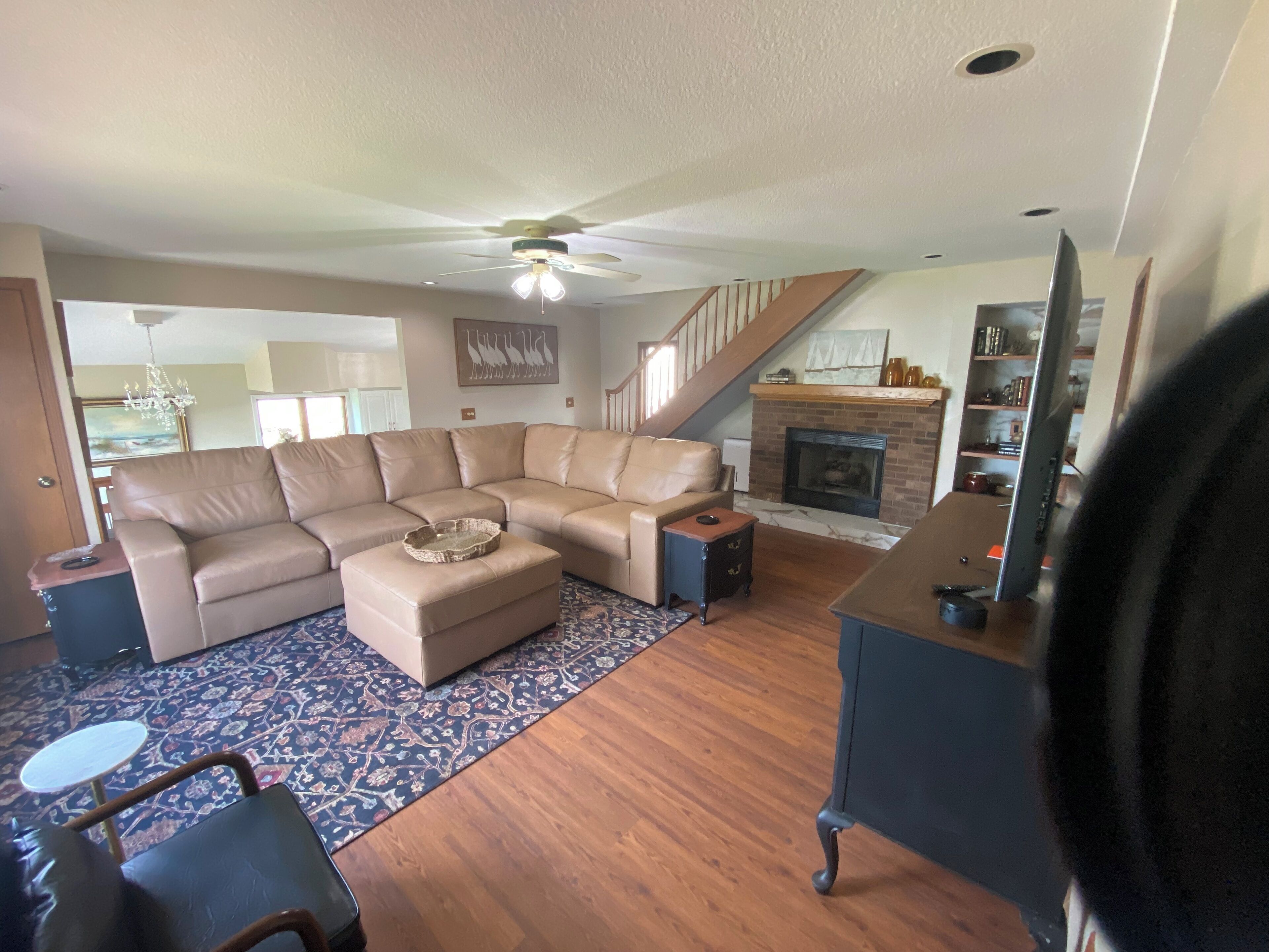 A living room with a sectional sofa, a small ottoman, a fireplace, and a staircase.